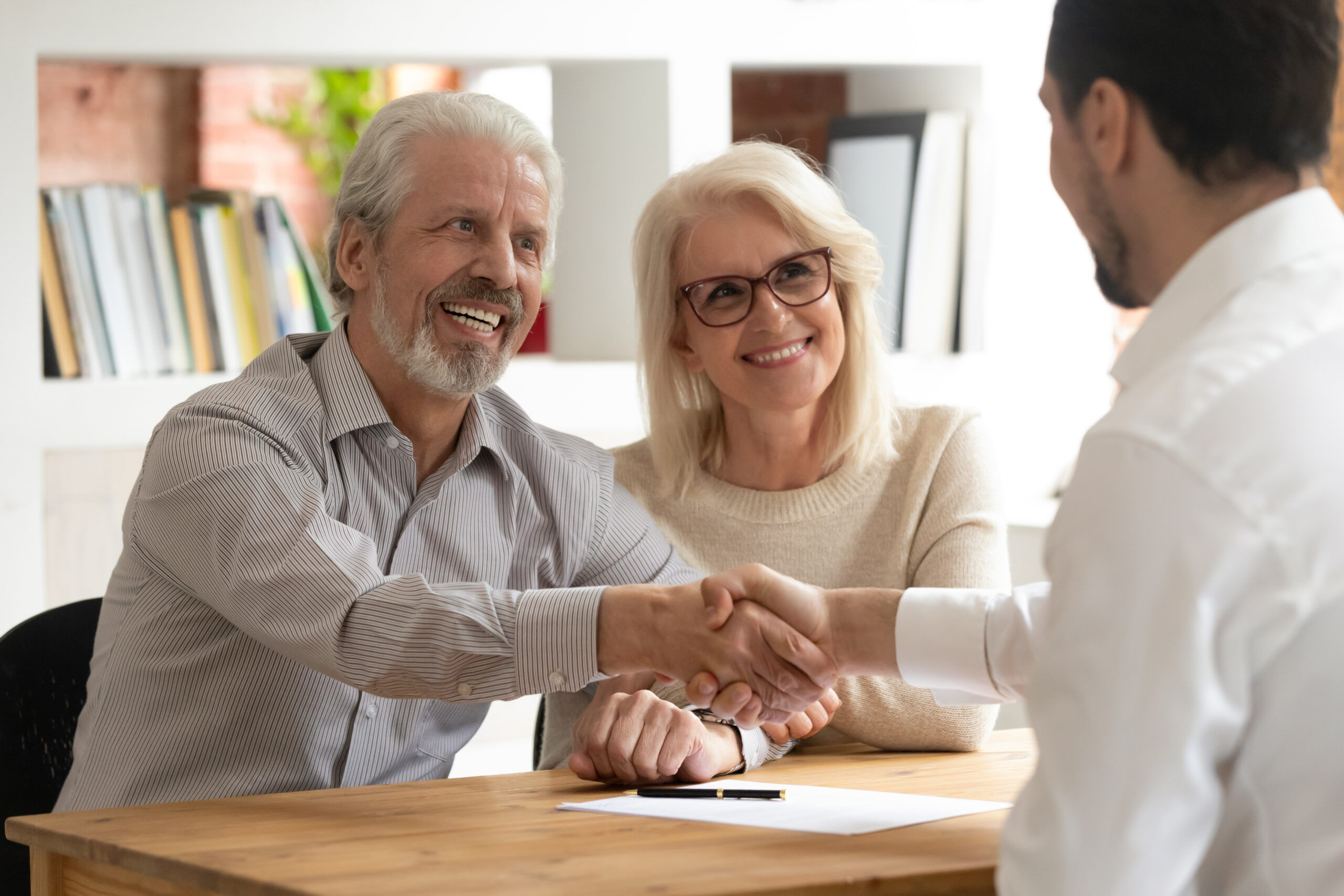 An elderly couple smiles and shakes hands with a professional