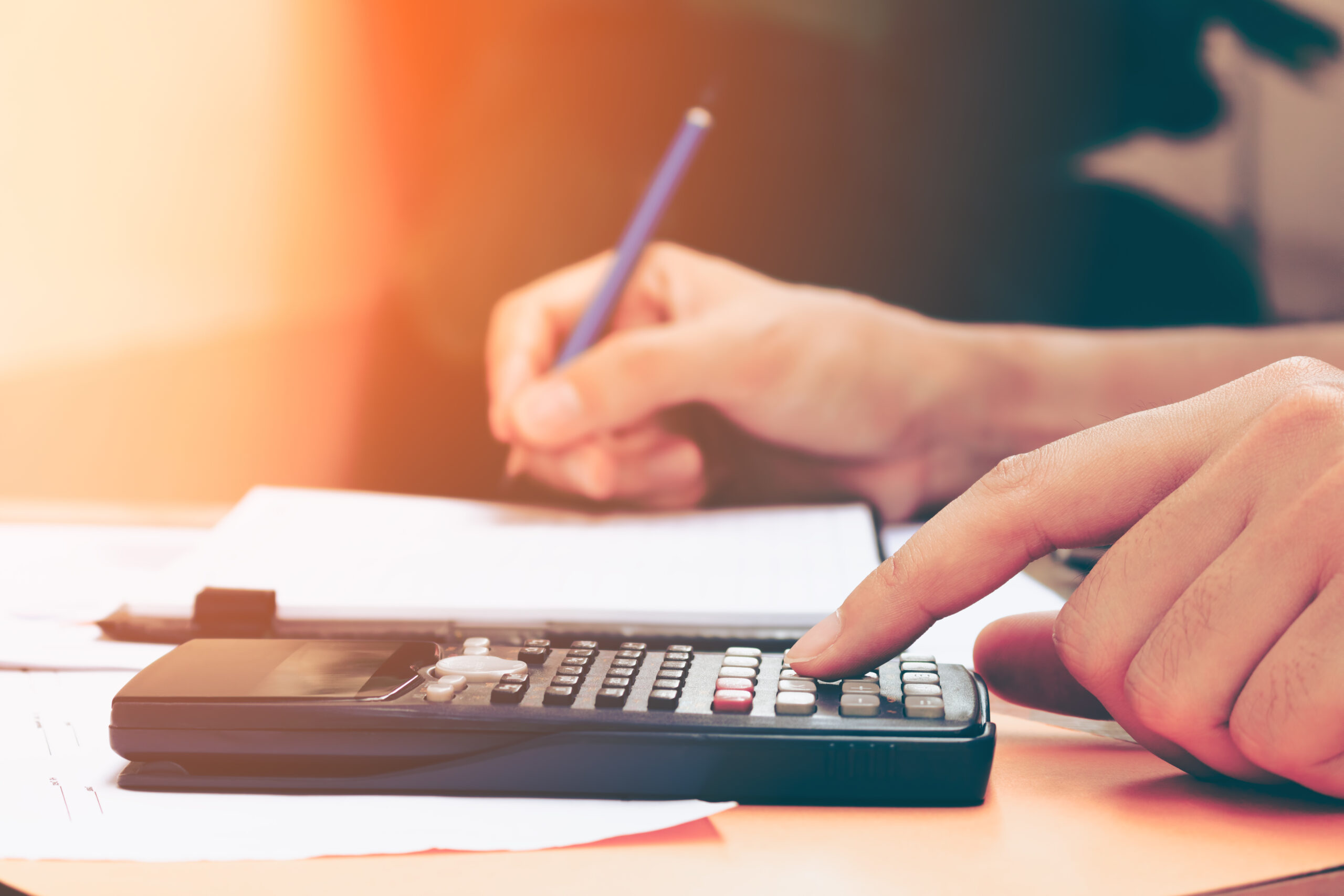A person calculates figures using a calculator while taking notes