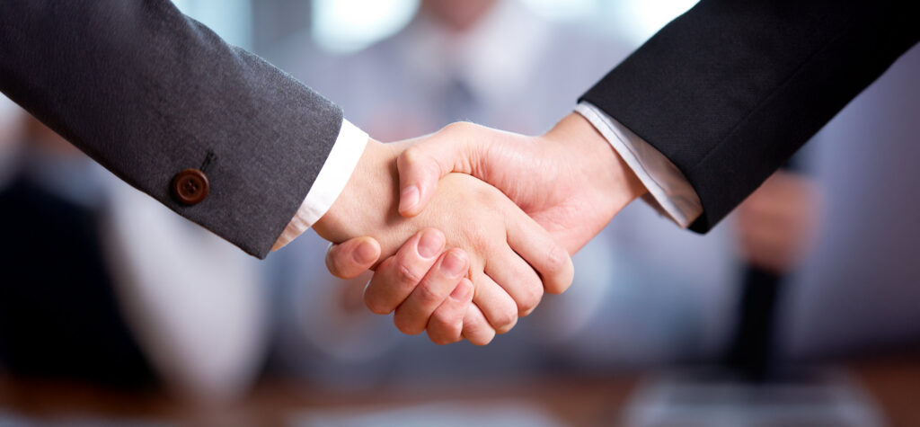 Two individuals in suits are shaking hands in a business setting